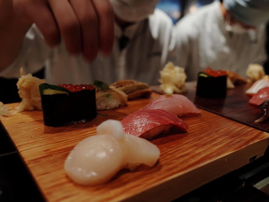 humà, persona, taula, taula de menjador, mobles, menjar, sushi, culinari, condiment, fusta, sèsam, beure, begudes, alcohol, sake, pasta, raviolis, dolços, pastisseria, fusta dura, menjar i beguda, frescor, carn, a l'interior, enfocament selectiu, primer pla, taula de tallar, preparació, material de fusta, persones incidentals, mida de la porció, menjar japonès, persones reals, carn de porc, natura morta, restaurant, menjar asiàtic, temptació, 4K