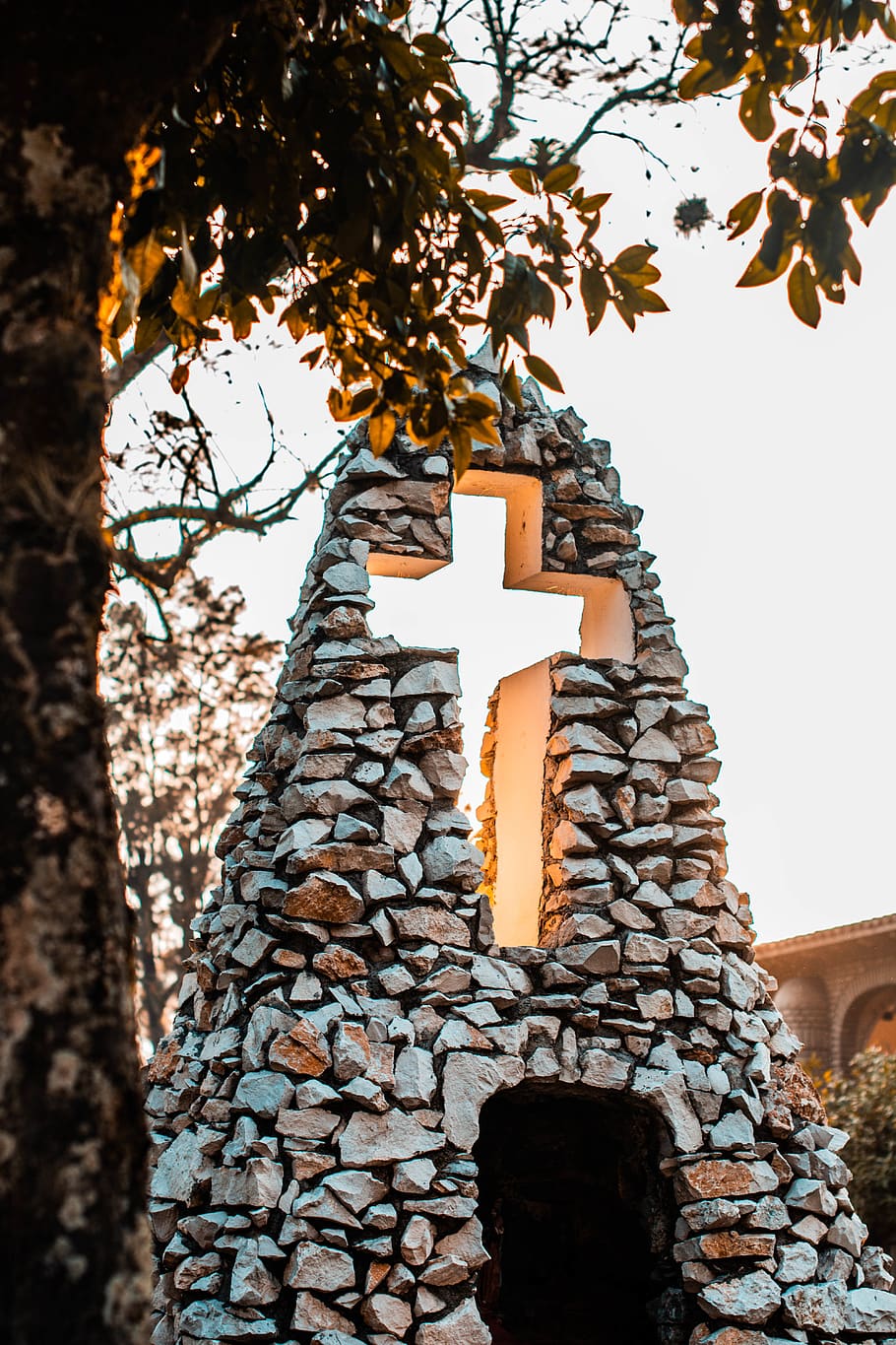 estàtua de formigó gris, arquitectura, color, construcció, creu, la llum del dia, disseny, fulles, llum, tir en angle baix, monument, a l'aire lliure, parc, roques, pedres, textura, viatjar, arbre, religió, creença, estructura construïda, vista d’angle baix, espiritualitat, lloc de culte, edifici, cap gent, planta, cel, dia, naturalesa, branca, exterior de l'edifici, material de pedra, paret de pedra, 5K