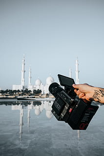 càmera de vídeo negra, humà, persona, pell, càmera, electrònica, edifici, arquitectura, fotògraf, fletxa, campanar, torre, càmera vermella, Abu Dhabi, fotografia, foto, ciutat, metròpolis, urbà, càmera de vídeo, mà humana, tecnologia, temes de fotografia, aigua, mà, part del cos humà, centrar-se en primer pla, cel, estructura construïda, càmera - equip fotogràfic, una persona, celebració, cel clar, exterior de l'edifici, còpia espai, persones reals, naturalesa, dia, càmera digital, 2K, CC0, domini públic, lliure de regalies
