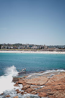 spiaggia, saltare, salto, immersione, tuffo, oceani, oceano, rocce, roccia, sabbia, fricchettone, gioventù, sole, estate, nuotare, acqua, cielo, mare, terra, architettura, esterno dell'edificio, cielo sereno, natura, giorno, struttura costruita, movimento, copia spazio, città, bellezza nella natura, all'aperto, onda, blu, costruzione, potere in natura, 5K, CC0, dominio pubblico, privo di copyright