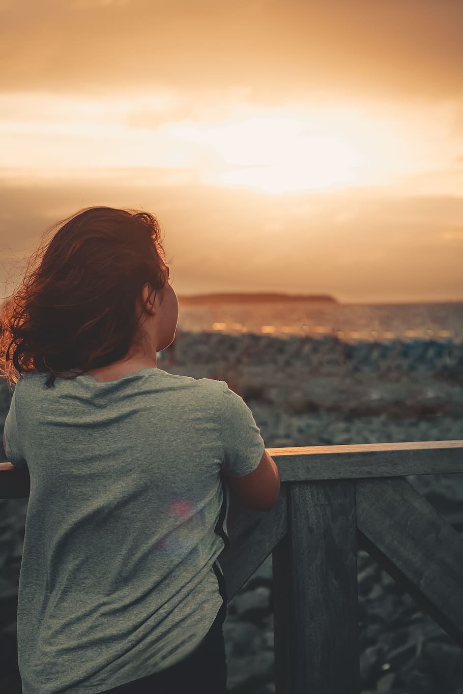 Frau, grau, Hemd mit Rundhalsausschnitt, Rückansicht, Dämmerung, Tageslicht, Person, Meer, Strand, Sonne, Sonnenuntergang, windig, Holzgeländer, Himmel, Wasser, eine Person, Geländer, echte Menschen, Lebensstile, Freizeitbeschäftigung, Szenen - Natur, Stehen, Schönheit in der Natur, Legere Kleidung, Natur, orange Farbe, Ruhe, draußen, Blick auf Ansicht, Horizont über Wasser, Frisur, 5K