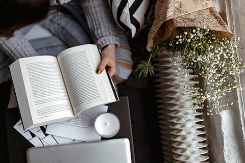 woman, sweater, reads, book, reading, reader, opened book, girl, female, lifestyle, relax, time, candle, pullover, jumper, one person, publication, holding, adult, midsection, indoors, women, hand, human hand, human body part, real people, sitting, young women, young adult, education, cup, leisure activity, day, 2K