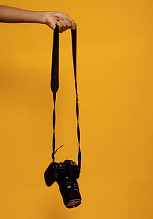 photo, person, holding, black, dslr camera, camera, camera lens, camera strap, dslr, hand, hold, lens, strap, human hand, human body part, one person, hanging, close-up, real people, studio shot, orange color, yellow, unrecognizable person, colored background, body part, indoors, finger, human finger, copy space, human arm, human limb, arms raised, orange background, 5K, CC0, public domain, royalty free