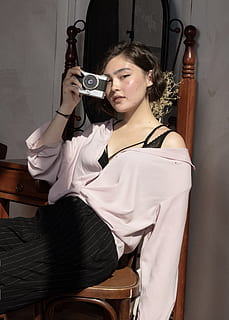 Câmera, eletrônicos, pessoa, humano, roupas, vestuário, design de interiores, dentro de casa, madeira, moda, vestido, vestido de noite, roupão, fotógrafo, câmera digital, câmera de vídeo, Madeira compensada, folhosa, calça, tela, uma pessoa, pessoas reais, sentado, adulto jovem, mulheres jovens, atividade de lazer, segurando, estilos de vida, assento, beleza, mulher bonita, comprimento de três quartos, roupa casual, Penteado, retrato, adulto, vista frontal, contemplação, 5K, CC0, domínio público, royalty free