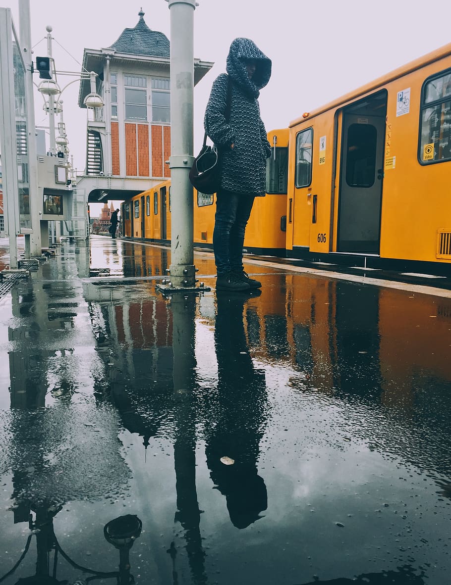 Alemanya, Berlín, ennuvolat, pluja, fantasmal, tren, groc, estació, figura, fosc, dessuadora, jaqueta, botes, hivern, fred, llum, reflexió, canviant d'humor, arquitectura, persones reals, una persona, aigua, exterior de l'edifici, estructura construïda, manera de transport, longitud completa, estils de vida, transport, humit, ciutat, temporada de pluges, bassal, de peu, a l'aire lliure, roba calenta, 2K