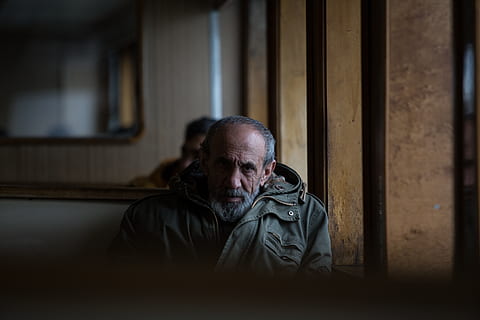 mand, sidder, inde, bygning, human, person, tøj, beklædning, ansigt, frakke, jakke, finger, overfrakke, skæg, ærme, dragt, hoved, senior borger, gelænder, træ, bregne, en person, rigtige mennesker, hanner, herrer, ansigtshår, indendørs, senior mænd, voksen, senior voksen, portræt, forfra, livsstil, hovedskud, modne mænd, taljen op, moden voksen, overvejelse, overskæg, 5K, CC0, offentligt domæne, royaltyfrie