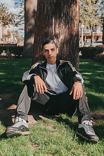 man, sitting, leaning, tree, clothing, apparel, footwear, shoe, person, human, plant, running shoe, grass, sleeve, fashion, sneaker, portrait, urban, long sleeve, tree trunk, vegetation, one person, casual clothing, nature, real people, lifestyles, leisure activity, full length, day, land, front view, looking at camera, field, young adult, teenager, outdoors, adolescence, teenage boys, contemplation, 4K, CC0, public domain, royalty free