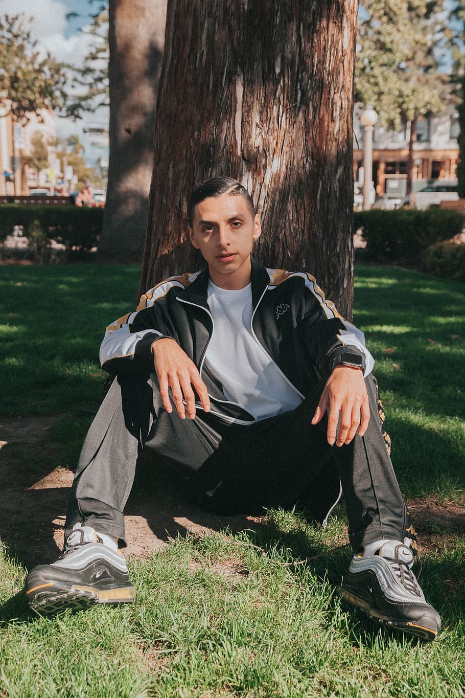 man, sitting, leaning, tree, clothing, apparel, footwear, shoe, person, human, plant, running shoe, grass, sleeve, fashion, sneaker, portrait, urban, long sleeve, tree trunk, vegetation, one person, casual clothing, nature, real people, lifestyles, leisure activity, full length, day, land, front view, looking at camera, field, young adult, teenager, outdoors, adolescence, teenage boys, contemplation, 4K
