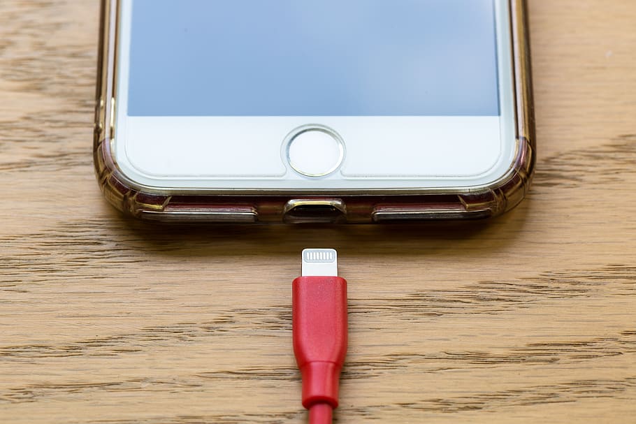 æble, iphone, teknologi, mobil, celle, cellulære, telefon, smartphone, kontor, meddelelse, forretning, skærm, usb, kabel, hjemknappen, touchscreen, forbindelse, stik, apparat, elektronisk, elektricitet, oplade, genoplade, batteri, rød, bord, indendørs, ingen mennesker, træ - materiale, smart telefon, bærbar informationsenhed, trådløs teknologi, stilleben, tæt på, enkelt objekt, høj vinkel visning, hvid farve, blå, direkte over, metal, dag, bærbar, blank, 5K