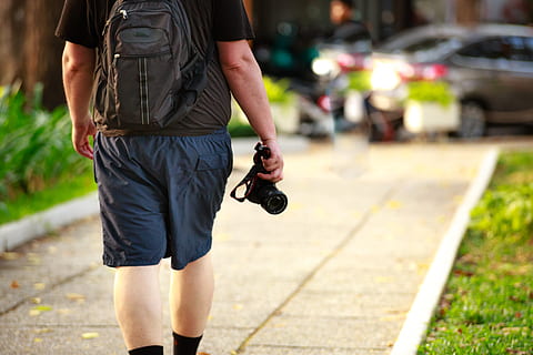 man, bezit, zwart, camera, rugzak, toevallig, apparaatje, gras, vrije tijd, levensstijl, buitenshuis, bestrating, persoon, fotograaf, fotografie, weg, straat, zomer, lopen, wandelen, slijtage, een persoon, focus op de voorgrond, casual kleding, stad, mannen, voetpad, echte mensen, achteraanzicht, staand, vrijetijdsbesteding, technologie, vervoer, dag, levensstijlen, camera - fotografische apparatuur, incidentele mensen, shorts, aan het wachten, 4K, CC0, publiek domein, royaltyvrij