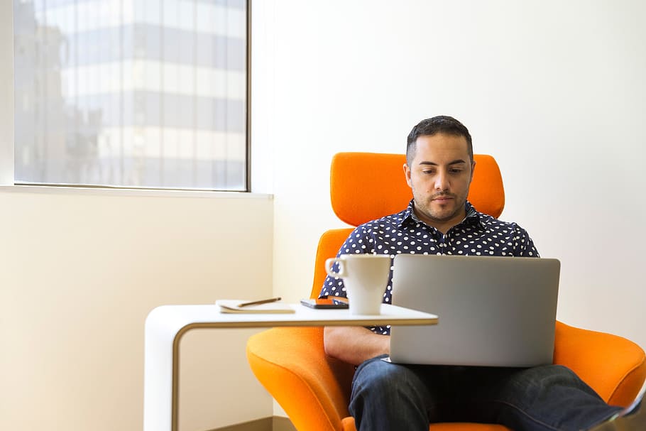 mand, skrivebord, macbook, computer, teknologi, forretning, hovedtelefoner, bærbar, kontor, mennesker, orange, stol, minimal, kaffe, kop, mad, arbejde, sidder, trådløs teknologi, bruger bærbar computer, meddelelse, forbindelse, en person, møbel, arbejder, herrer, voksen, indendørs, bord, forretningsmand, tre kvart længde, overvejelse, 5K