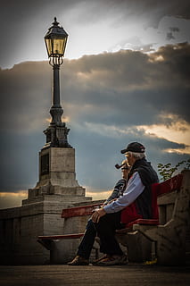 man, pipe, beside, woman, wearing, black, frame eyeglasses, day time, bench, clouds, cloudy, couple, elderly, lamppost, sitting, architecture, real people, cloud - sky, sky, full length, built structure, sculpture, lifestyles, statue, nature, art and craft, one person, travel destinations, human representation, history, leisure activity, the past, creativity, outdoors, 5K, CC0, public domain, royalty free