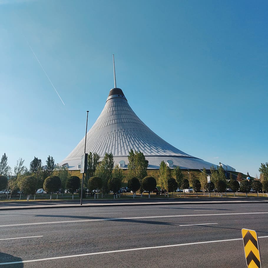 edifici gris de forma de con, carretera, torre, fletxa, campanar, arquitectura, edifici, metròpolis, urbà, ciutat, asfalt, astana, Kazakhstan, manera, intersecció, #mall #astana #khanshatyr, cúpula, planta, símbol, cel, estructura construïda, transport, marcatge de carreteres, exterior de l'edifici, dia, signe, marcatge, naturalesa, cap gent, arbre, cel clar, viatjar, blau, destinacions de viatge, a l'aire lliure, govern, 1080P