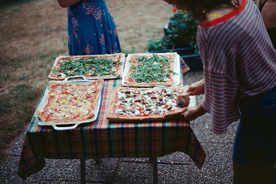 person, der serverer pizza, mad, pizza, person, human, måltid, hjem indretning, møbel, spisebord, bord, beklædning, tøj, kvinde, plante, dug, fad, søde sager, konfekture, kjole, pige, linned, mad og drikke, midsection, dag, friskhed, rigtige mennesker, herrer, fokus på forgrunden, sund kost, velvære, beholder, tilfældige mennesker, udendørs, bedrift, voksen, afslappet tøj, stående, 2K