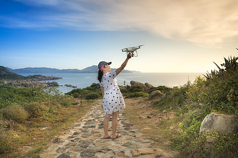 Foto, Frau, halten, Drohne, Strand, Wolken, Tageslicht, Drohnen-Kamera, weiblich, Dame, Landschaft, Freizeit, Berge, Ozean, draußen, Person, Polka Dot Kleid, Erholung, Entspannung, Felsen, Meer, seelandschaft, Himmel, Reise, Urlaub, weißes Kleid, Freizeitbeschäftigung, eine Person, echte Menschen, in voller Länge, Szenen - Natur, Lebensstile, wolke - himmel, Schönheit in der Natur, Natur, Land, Stehen, Wasser, Rückansicht, Pflanze, Legere Kleidung, ruhige Szene, menschlicher Arm, 5K, CC0, gemeinfrei, lizenzfrei