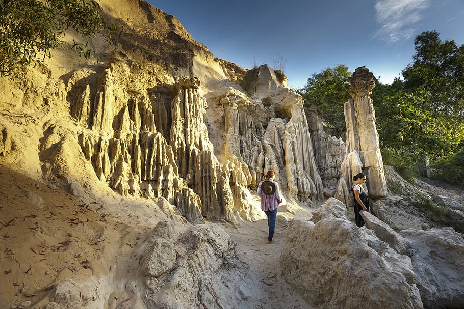 persona, caminar, terreny, cel blau, penya-segats, núvols, la llum del dia, durant el dia, medi ambient, erosió, formació geològica, geologia, paisatge, muntanya, naturalesa, a l'aire lliure, formacions rocoses, roques, rocós, escènic, vista, cel, pedres, turisme, arbres, dones, rock, rock - object, activitat d'oci, persones reals, sòlid, formació de roca, estils de vida, homes, una persona, bellesa a la natura, longitud completa, de peu, geografia física, adult, vista del darrere, viatjar, 5K
