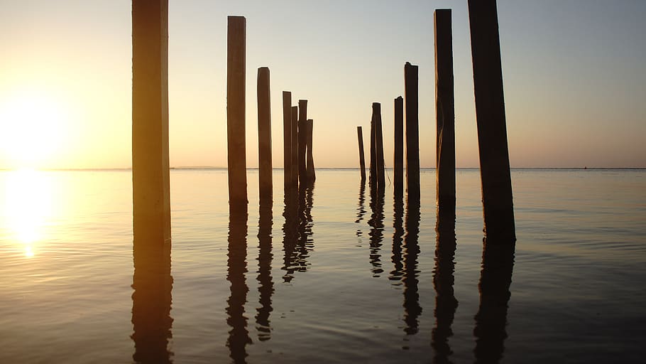 reflexió, posta de sol, platja, mar, pilars, or, marró, fusta, stand, sol brillar, llum del sol, ona tranquil·la, cel, aigua, naturalesa, tranquil·litat, arquitectura, horitzó sobre l’aigua, sol, davant del mar, estructura construïda, bellesa a la natura, horitzó, escenics - natura, escena tranquil·la, cap gent, cel clar, a l'aire lliure, post de fusta, gratacels, 5K