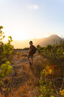 man carrying backpack, person, human, outdoors, nature, shorts, apparel, clothing, vegetation, plant, walking, field, land, leisure activities, adventure, countryside, hiking, people, grass, tree, road, full length, one person, leisure activity, sky, lifestyles, sunset, young adult, real people, beauty in nature, standing, casual clothing, mountain, scenics - nature, sunlight, adult, landscape, young women, 5K, CC0, public domain, royalty free