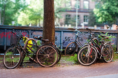 parc de bicicletes, bicicleta, transport, vehicle, Berlín, Alemanya, prenzlauer berg, verd, a l'aire lliure, carrer, bokeh, bloquejat, bloqueig, ciutat, motor, màquina, cicle, viatjar, manera de transport, arbre, dia, vehicle terrestre, planta, arquitectura, cap gent, estacionari, naturalesa, estructura construïda, tronc de l'arbre, tronc, centrar-se en primer pla, exterior de l'edifici, barana, roda, 4K, CC0, domini públic, lliure de regalies