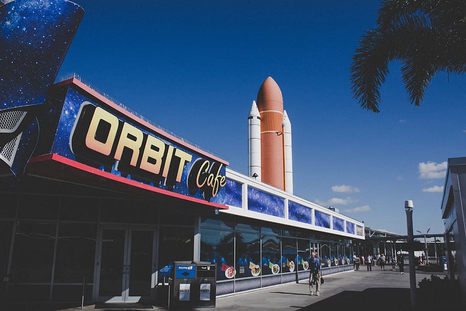 cafè orbital, durant el dia, persona, humà, transport, avions, vehicle, nau espacial, transbordador espacial, orlando, centre d’espai kennedy, bicicleta, avió, avió de línia, Camí, a l'aire lliure, naturalesa, coet, menjar, carretera, arquitectura, estructura construïda, text, comunicació, cel, signe, exterior de l'edifici, ciutat, guió occidental, vista d’angle baix, carrer, cel clar, blau, grup de persones, edifici, viatjar, dia, columna arquitectònica, 5K
