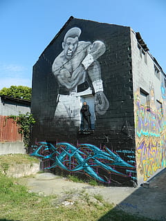 human, person, kunst, graffiti, vægmaleri, maleri, væg, beklædning, frakke, tøj, overfrakke, køretøj, transportmidler, mursten, cykel, sidder, shorts, bunker, bygning, Kunst og håndværk, arkitektur, repræsentation, kreativitet, menneskelig repræsentation, bygget struktur, mandlig lighed, skulptur, statue, dag, bygning udvendig, håndværk, himmel, natur, mennesker, fuld længde, murbygningsfunktion, udendørs, 4K, CC0, offentligt domæne, royaltyfrie