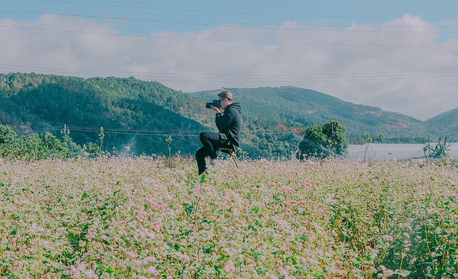 mand, sidder, midten, blomsterfelt, ved brug af, sort, dslr kamera, skyer, dyrkede arealer, dagslys, miljø, gård, Mark, flora, blomster, bakke, hobby, landskab, fritid, bjerg, natur, person, fotograf, naturskøn, sommer, tager billeder, træer, arbejde, rigtige mennesker, livsstil, en person, plante, fritidsaktivitet, skønhed i naturen, scenics - natur, ikke-urbane scene, herrer, dag, vækst, fuld længde, himmel, afslappet tøj, ro, aktivitet, jord, udendørs, modne mænd, 5K