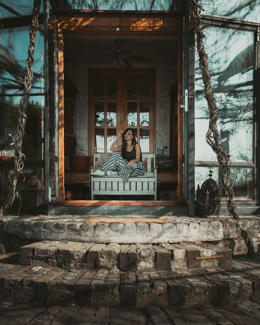 dona, assegut, banc, diseny arquitectònic, arquitectura, maons, la llum del dia, durant el dia, disseny, porta, entrada, exterior, casa exterior, frontal, casa, exterior de casa, a l'interior, endins, paisatge, a l'aire lliure, paviment, persona, propietat, estat real, residencial, pedres, urbà, paret, fusta, porta de fusta, una persona, vista frontal, estructura construïda, persones reals, retrat, adult jove, activitat d'oci, estils de vida, representació, representació humana, mirant la càmera, dia, finestra, roba casual, adult, 4K