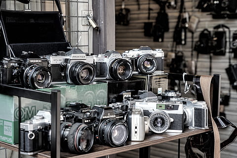 Elektronik, Kamera, Digitalkamera, Videokamera, Leichtmetallfelge, Rad, Maschine, gesprochen, Kameraobjektiv, Regal, Gurt, Reifen, Objektivkappe, Sperrholz, Holz, Fußboden, Fahrzeug, Transport, Zug, Lokomotive, Technologie, Kamera - Fotoausrüstung, Fotografie-Themen, Retro-Stil, Objektiv - optisches Instrument, Nahansicht, keine Leute, Antiquität, zu verkaufen, Einkaufen, drinnen, Fokus auf den Vordergrund, Fotoausrüstung, Stillleben, Ausrüstung, Filmkamera, Tag, Sammlung, große gruppe von gegenständen, silberfarben, 5K, CC0, gemeinfrei, lizenzfrei