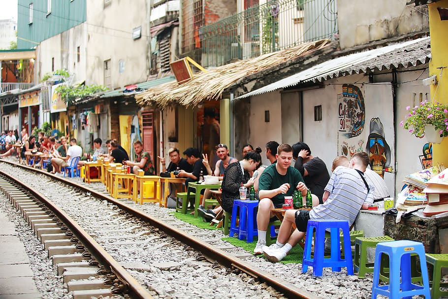 gent, al costat, tren ferroviari, arquitectura, comerç, multitud, la llum del dia, grup, homes, a l'aire lliure, vies del ferrocarril, senyalització, assegut, femta, botigues, turisme, turistes, ciutat, urbà, gran grup de persones, persones reals, grup de persones, estructura construïda, exterior de l'edifici, dones, adult, pista, estils de vida, dia, transport per ferrocarril, edifici, taula, esperant, 5K