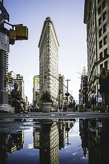 Basso, fotografia ad angolo, edificio di ferro da stiro, costruzione, pozzanghera, riflessione, persona, sat, seduta, all'aperto, architettura, punto di riferimento, grattacielo, pomeriggio, soleggiato, paesaggio urbano, orizzonte, destinazione del viaggio, iconico, Flatiron, Manhattan, cielo, scena urbana, struttura costruita, città, skyline urbano, acqua, esterno dell'edificio, posto famoso, distretto del centro, Stati Uniti d'America, fiume, moderno, vita di città, giorno, 5K, CC0, dominio pubblico, privo di copyright