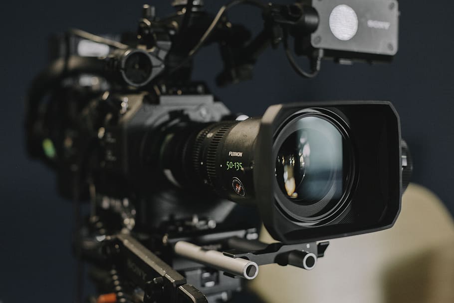 schwarze Schulterkamera, Technologie, Filmindustrie, Fernsehkamera, Objektiv - optisches Instrument, Kamera - Fotoausrüstung, Fotografie-Themen, Kunst, Kultur und Unterhaltung, drinnen, Nahansicht, Film, Linse - Auge, Fokus auf den Vordergrund, Filmkamera, Industrie, Heimvideokamera, die Medien, Video, Studio, Rundfunk-, Studioaufnahme, Dreharbeiten, Digitalkamera, schwarzer Hintergrund, Kameramann, 5K