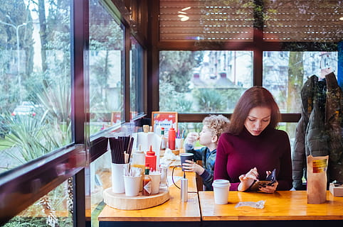 woman, sitting, beside, table, using, phone, child, coffee, condiments, dining, eat, eating, HEROESBRIEF, indoors, inside, jacket, kid, people, restaurant, seat, son, texting, real people, young adult, young women, food and drink, lifestyles, casual clothing, one person, leisure activity, adult, waist up, women, front view, window, drink, smiling, glass, 5K, CC0, public domain, royalty free