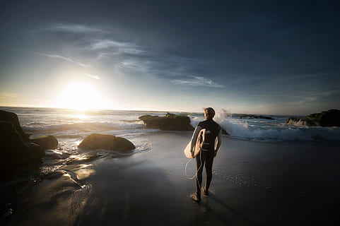 platja, home, oceà, roques, sorra, mar, paisatge marí, vora del mar, cel, sol, sol brillant, posta de sol, taula de surf, surfista, aigua, onades, longitud completa, de peu, una persona, bellesa a la natura, escenics - natura, persones reals, núvol - cel, activitat d'oci, naturalesa, estils de vida, terra, rock, adult jove, horitzó sobre l’aigua, a l'aire lliure, 4K, CC0, domini públic, lliure de regalies
