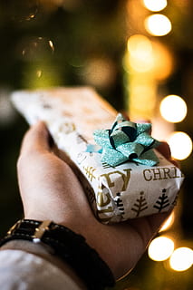 white gift box, gift, human, person, wristwatch, finger, lights, present, christmas, hand, plectrum, diwali, funeral, life buoy, sphere, flame, fire, wrist, flower, blossom, plant, human hand, one person, real people, human body part, close-up, holding, focus on foreground, lifestyles, illuminated, leisure activity, celebration, men, personal perspective, unrecognizable person, body part, indoors, selective focus, adult, 2K, CC0, public domain, royalty free