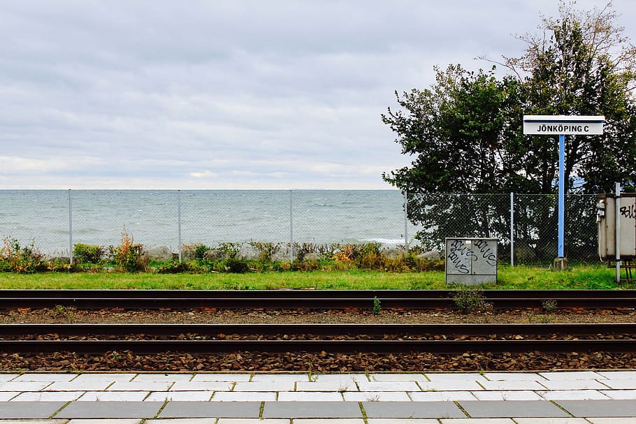 Suécia, Jonköping, agua, estação, Ferrovia, lago, Transporte ferroviário, céu, rastrear, nuvem - céu, transporte, natureza, modo de transporte, dia, ninguém, transporte público, plataforma de estação de trem, comunicação, placa, plantar, arquitetura, estação ferroviária, árvore, ao ar livre, 5K