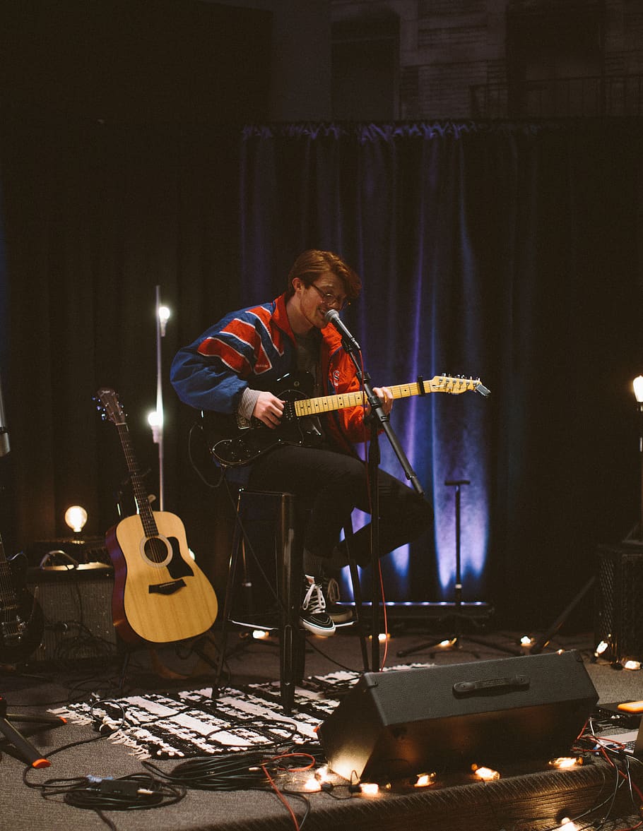 mand, sang, spille, guitar, person, human, musikinstrument, fritids aktiviteter, musiker, menneskemængde, guitarist, performer, koncert, scene, Rock koncert, elektrisk guitar, belysning, musik band, lut, basguitar, møbel, sofa, eventyr, musik, kunstkultur og underholdning, streng instrument, musikalsk udstyr, ydeevne, indendørs, kunstner, en person, rigtige mennesker, herrer, belyst, scene - ydeevne plads, mikrofon, afslappet tøj, rockmusik, akustisk guitar, mikrofonstativ, lys, plukning af et instrument, underholdning besættelse, 4K