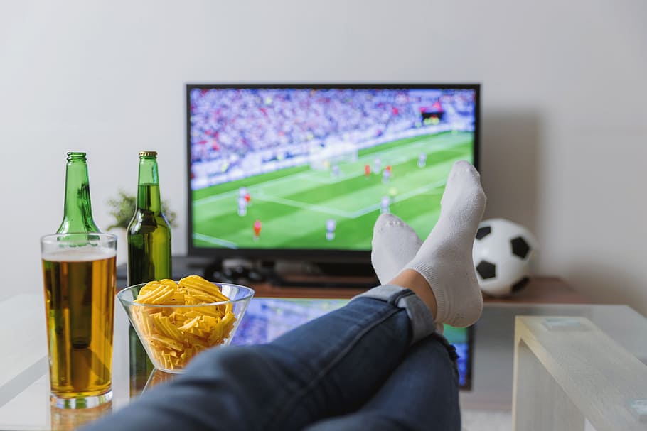mirant, futbol, coincidir, televisió, peus, taula., esport d’equip, esport, part del cos humà, televisor, activitat d'oci, pilota de futbol, a l'interior, equipament esportiu, una persona, mà humana, cova d’home, tecnologia, estils de vida, mirant la televisió, mà, alcohol, adult, relaxació, cervesa - alcohol, part del cos, extremitat humana, pantalla plana, 5K