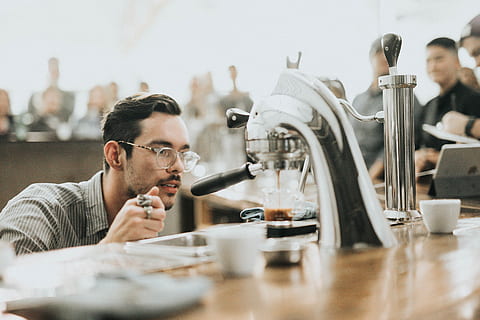coffee, maker, machine, hot, drink, brewed, espresso, table, people, man, guy, barista, coffeehouse, shop, business, adult, headshot, men, one person, indoors, working, mid adult, sitting, portrait, real people, glasses, mid adult men, young men, food and drink, concentration, selective focus, 2K, CC0, public domain, royalty free