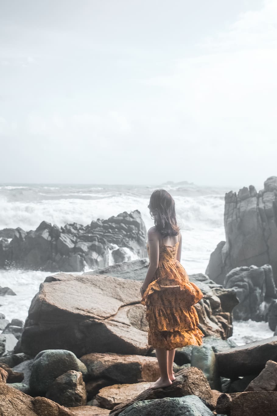 dona, taronja, vestit, de peu, roques de roca, platja, núvols, Costa, la llum del dia, durant el dia, medi ambient, femella, noia, horitzó, paisatge, mamífer, naturalesa, oceà, costa d’oceà, persona, pose, roques, rocós, costa rocosa, escènic, mar, vora del mar, Riba, cel, pedres, aigua, onades, vestit groc, rock, rock - object, sòlid, vista del darrere, longitud completa, terra, una persona, estils de vida, escenics - natura, persones reals, bellesa a la natura, activitat d'oci, horitzó sobre l’aigua, a l'aire lliure, mirant la vista, pentinat, 4K