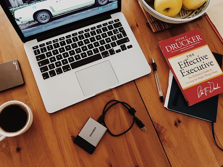 escriptori, ordinador, espai de treball, lloc de treball, treballar, aixafar-lo, disc dur, treball dur, cafè, llibre, PC, mac, bolígraf, quadern, MacBook, taula, fusta, taula de fusta, teclat, tecnologia sense fils, comunicació, tecnologia, connexió, dispositiu d’informació portàtil, portàtil, telèfon intel·ligent, material de fusta, telèfon mòbil, a l'interior, vista d’angle alt, tassa, natura morta, beure, portabilitat, cap gent, mobles, text, 4K