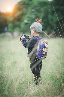 ragazzo, portando, zaino, detenzione, telecamera, in piedi, verde, erba, berretto, bambino, carina, tempo libero, persona, ricreazione, indossare, giovane, infanzia, una persona, campo, pianta, persone reali, terra, giorno, natura, rappresentazione, attività di svago, lunghezza intera, concentrarsi sulle conoscenze acquisite, giocattolo, stili di vita, vista frontale, capi di abbigliamento, all'aperto, innocenza, 5K, CC0, dominio pubblico, privo di copyright
