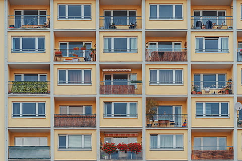 braunes Betongebäude, Balkon, Fenster, Wohnung, Komplex, Gebäude, Fassade, Zuhause, Außen, Leben, städtisch, Stadt, Muster, symmetrisch, Symmetrie, Haus, architektonisch, die Architektur, Gebäudehülle, gebaute Struktur, Wohngegend, keine Leute, Vollbild, Hintergründe, Glas - Material, Tag, Seite an Seite, draußen, in einer Reihe, Sonnenlicht, Reflexion, Flachwinkelansicht, Wiederholung, Gelb, Reihenhaus, Fensterrahmen, 5K, CC0, gemeinfrei, lizenzfrei