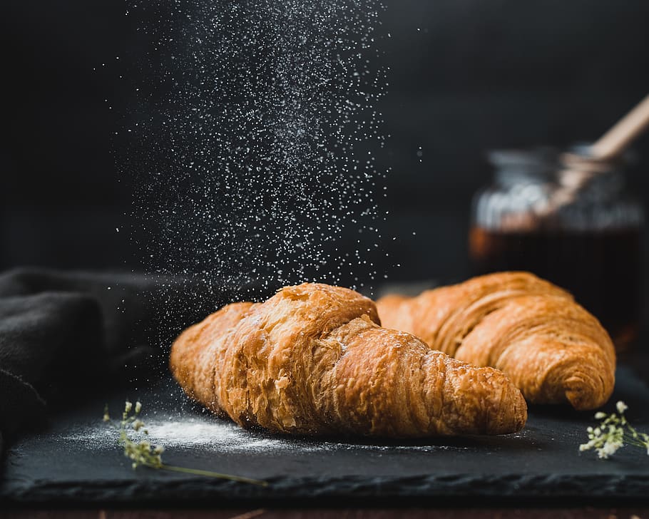 zwei braune Croissants, Lebensmittel, Essen und Trinken, Croissant, gebacken, französisches Essen, Frische, Nahansicht, drinnen, keine Leute, Brot, fertig für den Verzehr, Fokus auf den Vordergrund, Süßes Essen, gebackenes Gebäck, selektiver Fokus, Brötchen, Stillleben, braun, Geschäft, Tabelle, schwarzer Hintergrund, Frühstück, Puderzucker, Snack, Backblech, 2K
