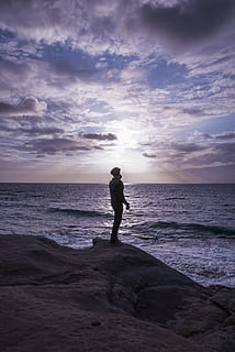 Foto, Mann, Stehen, Felsformation, hinterleuchtet, Strand, Wolken, wolkig, Dämmerung, Tageslicht, Umgebung, Horizont, idyllisch, Natur, Ozean, friedlich, Person, Erholung, Wellen, Landschaft, szenisch, Meer, seelandschaft, still, Wasser, Himmel, wolke - himmel, Land, eine Person, Horizont über Wasser, Schönheit in der Natur, Szenen - Natur, echte Menschen, Freizeitbeschäftigung, Sonnenuntergang, in voller Länge, Lebensstile, draußen, 4K, CC0, gemeinfrei, lizenzfrei