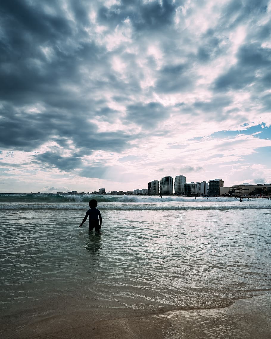 nen, vora del mar, platja, noi, edificis, núvols, alba, la llum del dia, horitzó, paisatge, oci, oceà, gent, recreació, reflexió, escènic, mar, cel, estiu, posta de sol, aigua, onades, núvol - cel, persones reals, exterior de l'edifici, una persona, arquitectura, davant del mar, naturalesa, estructura construïda, silueta, ciutat, bellesa a la natura, homes, activitat d'oci, de peu, terra, a l'aire lliure, 4K