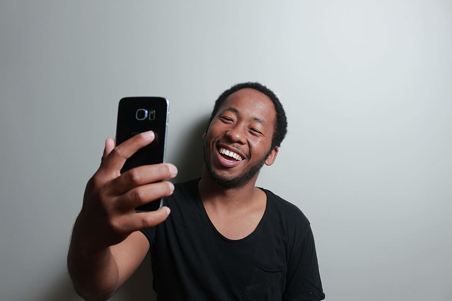 home, celebració, smartphone, inclinat, blanc, paret, expressió facial, diversió, retrat, selfie, somriu, tecnologia, telèfon intel·ligent, telèfon mòbil, tecnologia sense fils, dispositiu d’informació portàtil, comunicació, felicitat, somrient, vista frontal, tir de l'estudi, una persona, emoció, telèfon, gris, connexió, a l'interior, utilitzant el telèfon, fons gris, tirada al cap, 4K