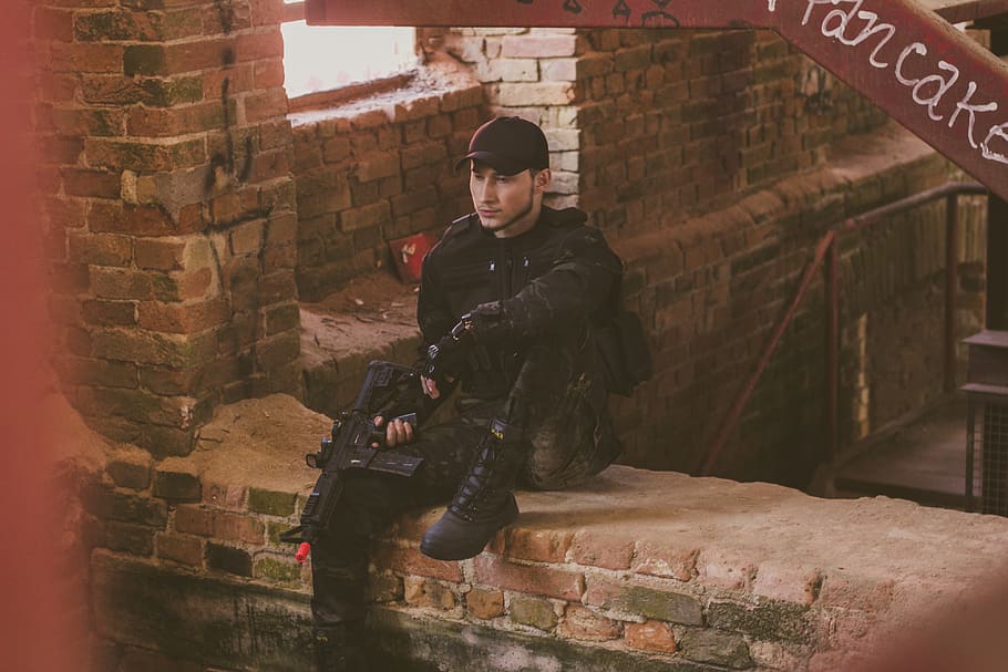 uomo, detenzione, pistola giocattolo, mattoni, persona, uniforme, arma, indossare, persone reali, una persona, architettura, capi di abbigliamento, attività di svago, struttura costruita, lunghezza intera, stili di vita, mattone, giovani uomini, parete, giorno, giovane adulto, vista frontale, esterno dell'edificio, muro di mattoni, uomini, maschi, ritratto, all'aperto, governo, 4K