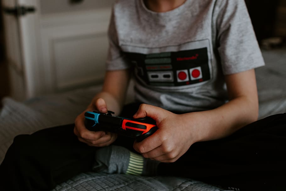 ragazzo, seduta, grigio, letto, giocando, detenzione, tecnologia, Sezione centrale, abbigliamento casual, una persona, comunicazione, tecnologia wireless, in casa, stili di vita, uomini, bambino, ragazzi, persone reali, dispositivo di informazione portatile, infanzia, attività di svago, maschi, vista frontale, video gioco, adolescente, 5K