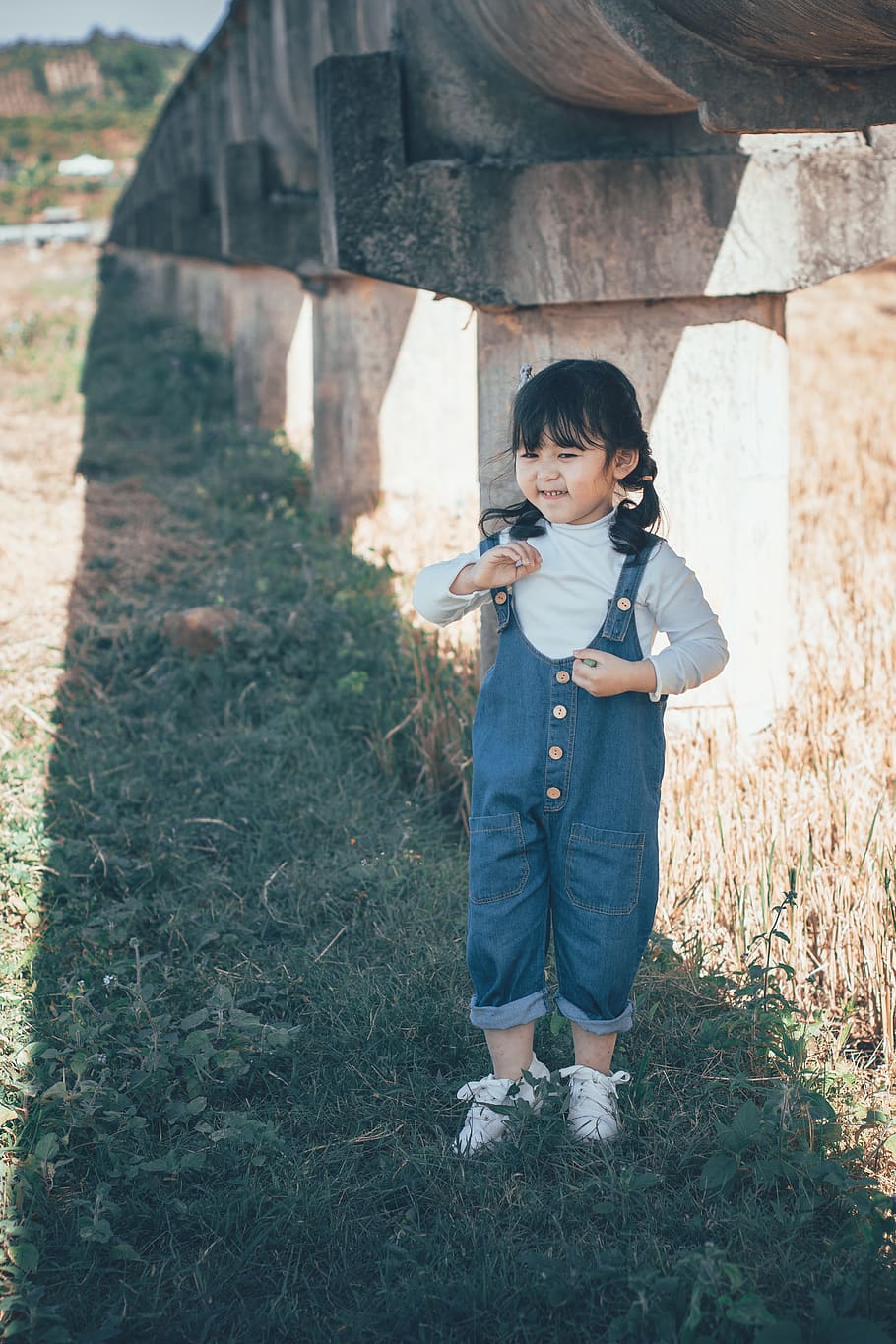 menina, de pé, concreto, estrutura, franja, criança, fofa, luz do dia, campo, Diversão, grama, jeans, lazer, pequeno, macacão, pessoa, tranças, sombra, sorridente, verão, vestem, infância, comprimento total, plantar, uma pessoa, roupa casual, terra, natureza, pessoas reais, atividade de lazer, Rapazes, segurando, dia, machos, estilos de vida, vista frontal, ao ar livre, inocência, 5K