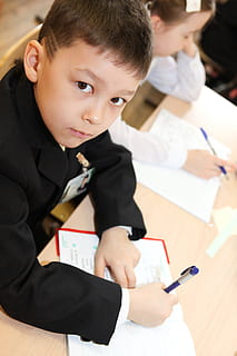noi, nen, infància, aula, educació, educatiu, aprendre, escola, alumne, petit, fill, estudiant, estudiar, pensar, joventut, nois, homes, mascles, celebració, a l'interior, persones reals, paper, assegut, taula, aprenentatge, escriure, concentració, centrar-se en primer pla, bolígraf, material escolar, innocència, uniforme, bloc de notes, 2K, CC0, domini públic, lliure de regalies